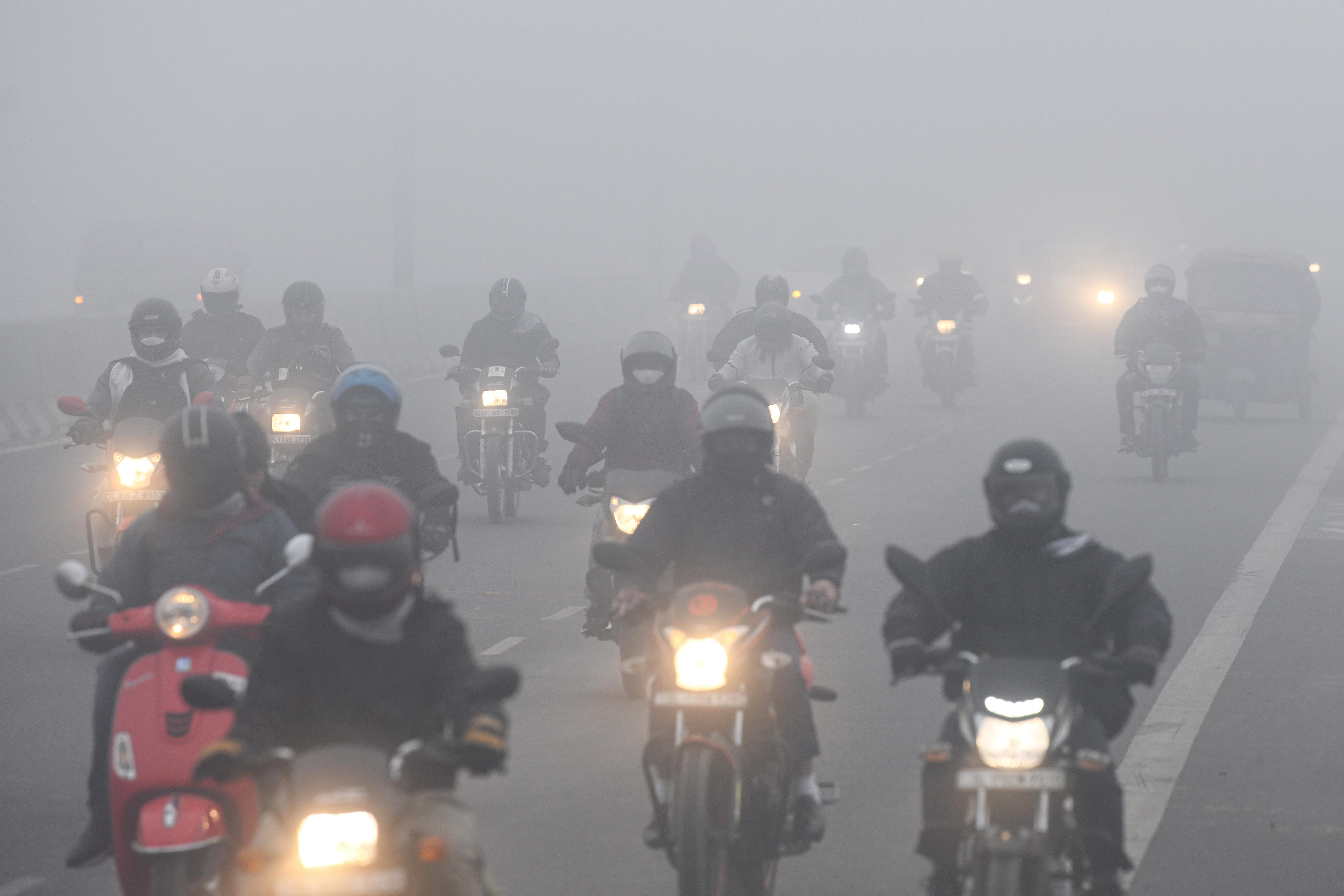 Vehicles ply on a road amid dense fog