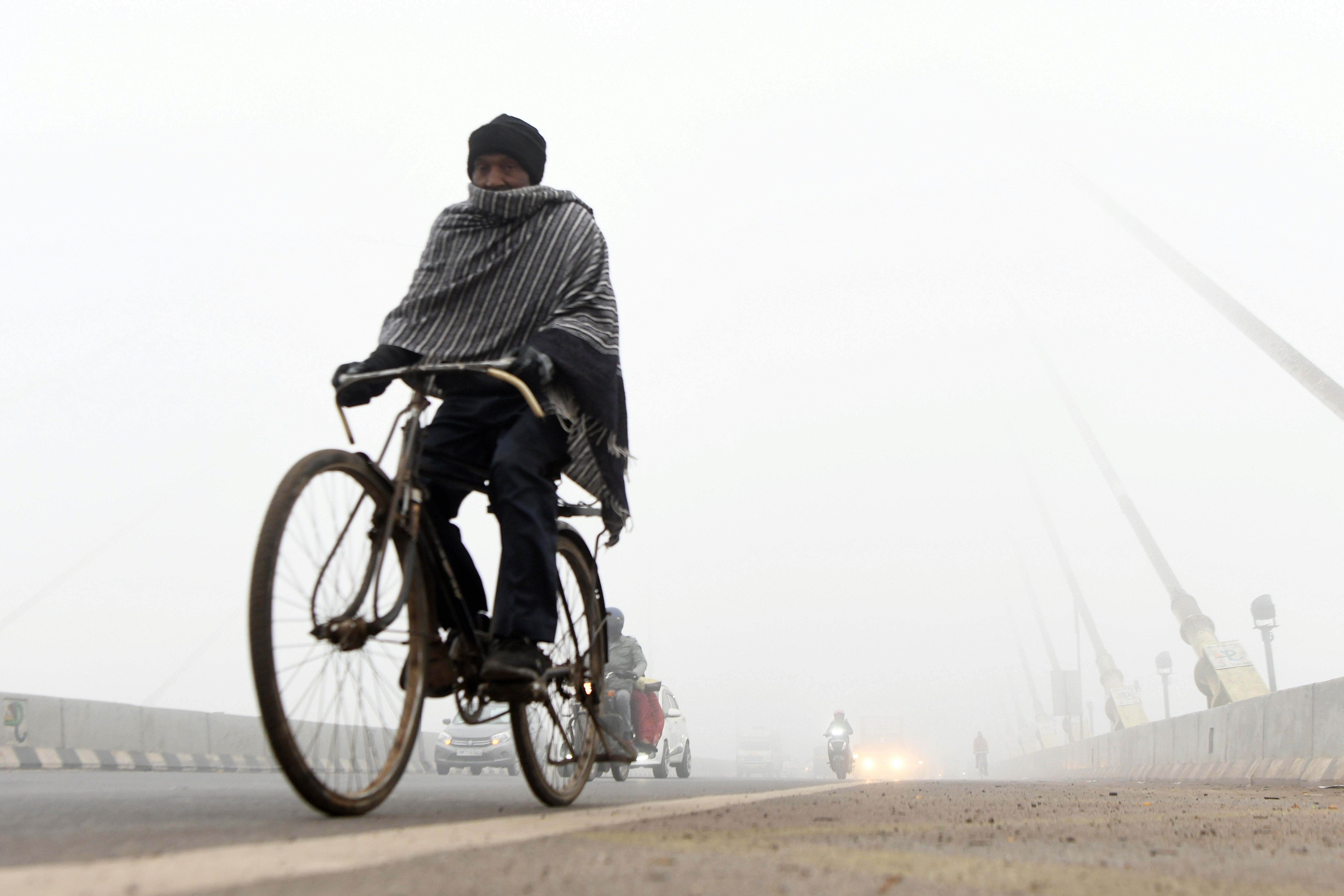 A man paddles his bicycle amid dense fog