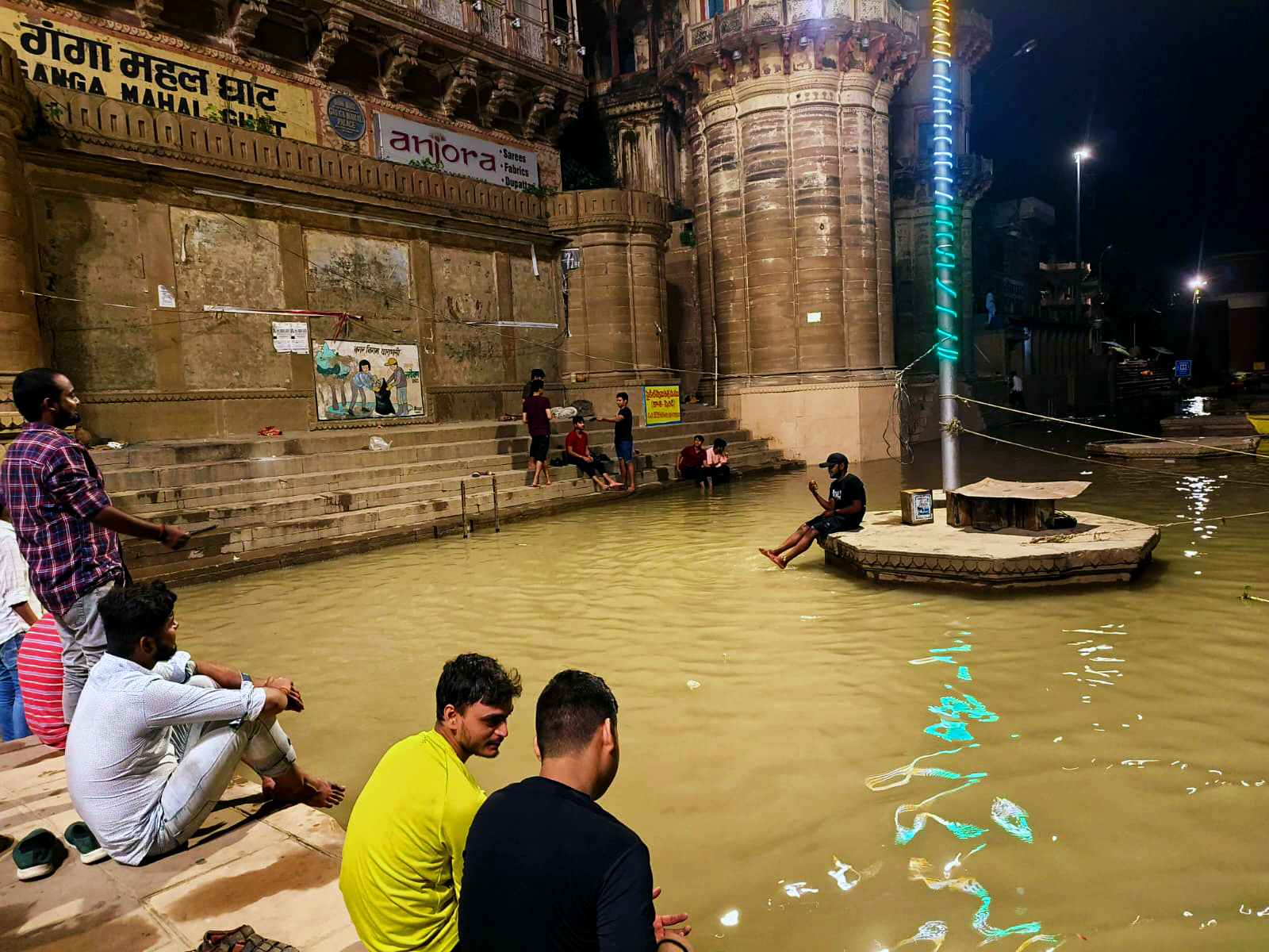 People sit on the banks of swollen Ganga river following heavy rainfall at Ganga Mahal Ghat